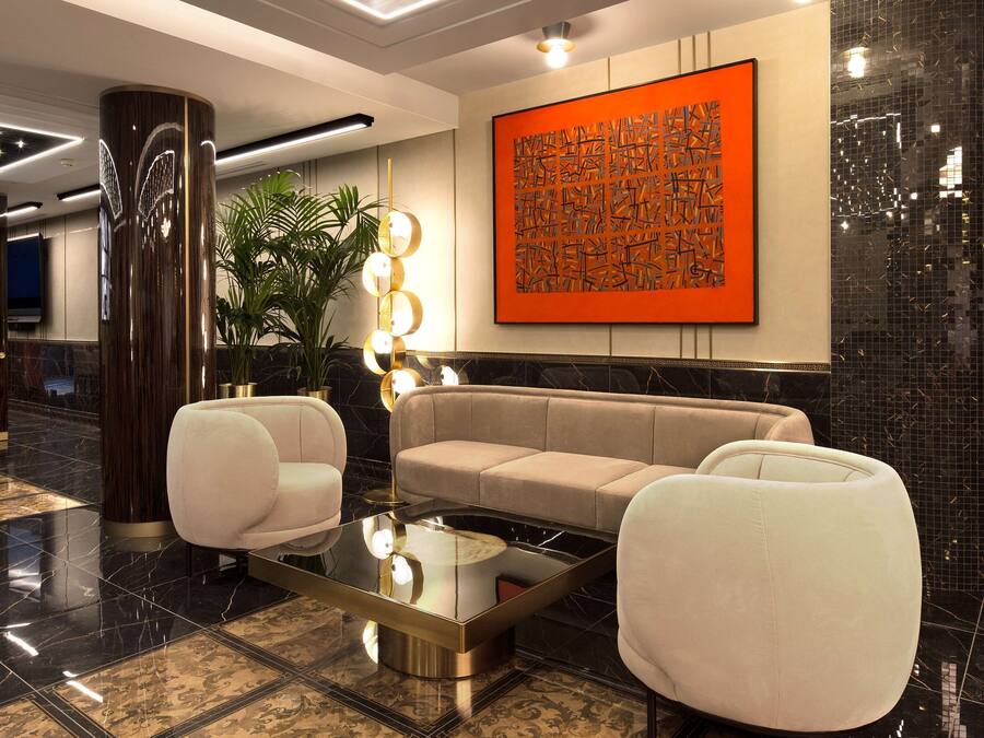 Un vestíbulo moderno con un sofá modular, dos sillones, una mesa de centro de vidrio y un cuadro abstracto de gran tamaño en la pared.
