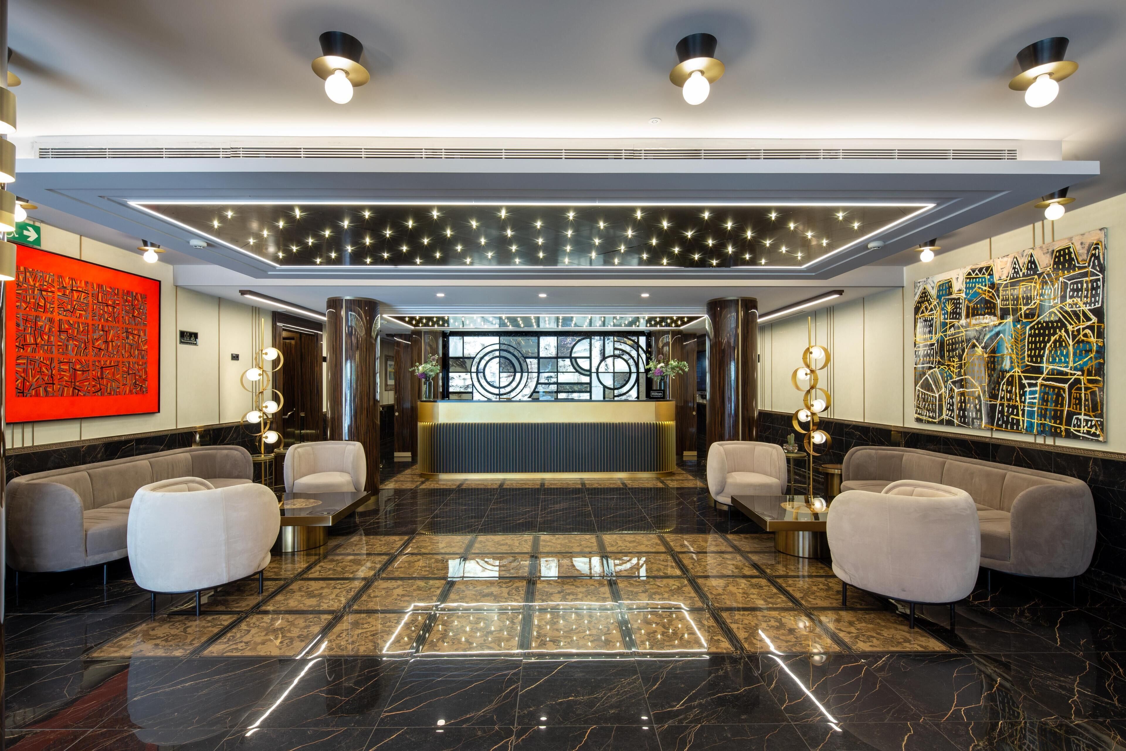 A hotel lobby with a reception desk, seating area, and decorative lighting.