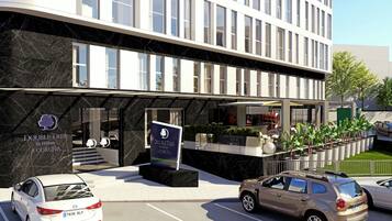 Un hotel moderno con fachada de mármol, un cartel y un estacionamiento con coches.