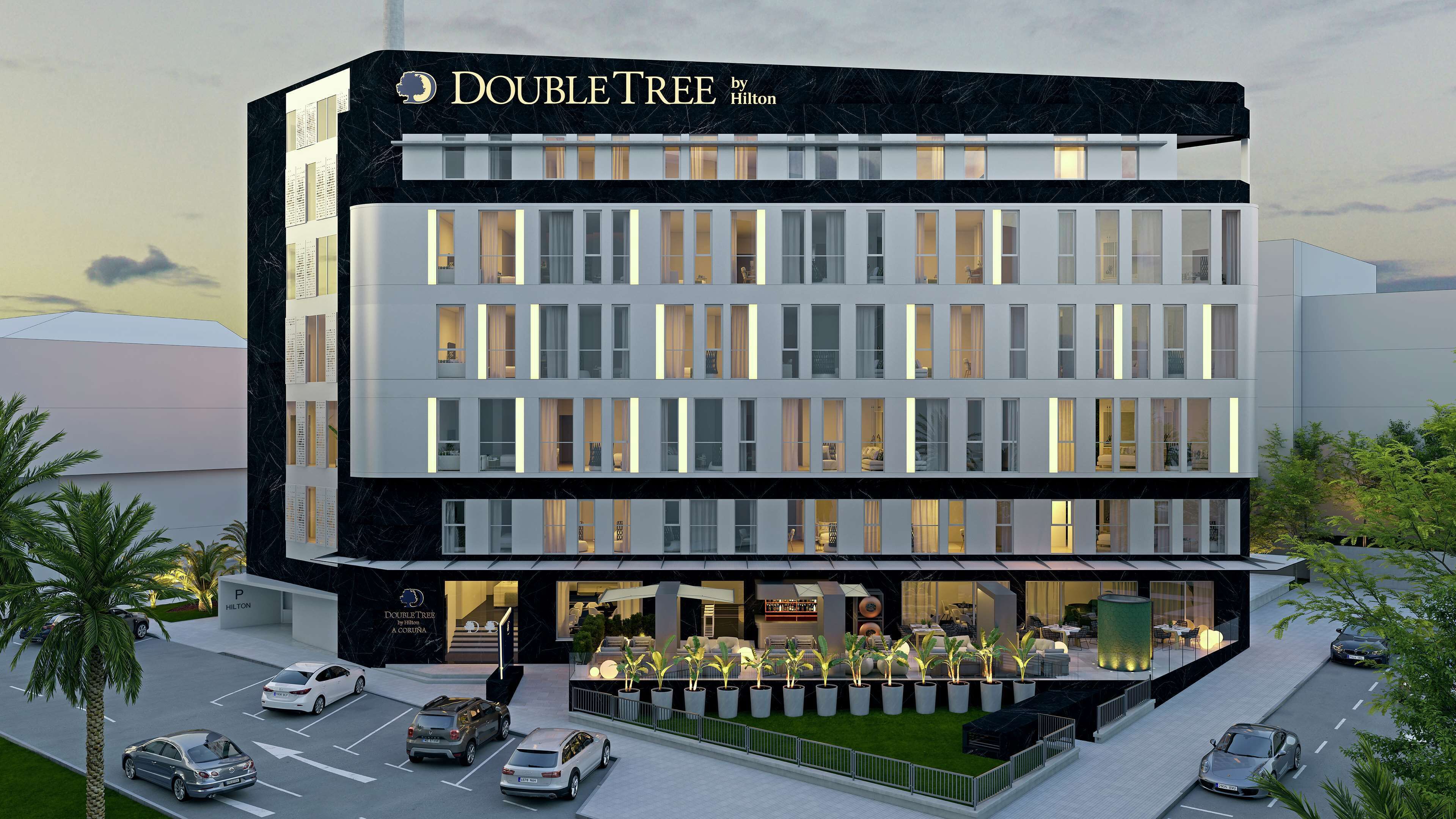 Un moderno edificio de hotel con un llamativo letrero de "DOUBLE TREE by Hilton", varios pisos y una zona de entrada bien iluminada con asientos al aire libre.