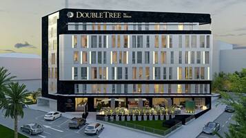 Un moderno edificio de hotel con un llamativo letrero de "DOUBLE TREE by Hilton", varios pisos y una zona de entrada bien iluminada con asientos al aire libre.