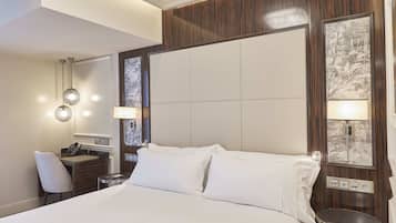 Habitación de hotel con una cama grande, un escritorio con silla, una mesita pequeña y una lámpara de pared.