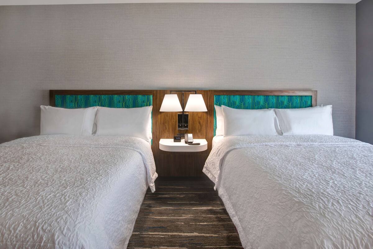 A hotel room with two single beds, a nightstand with a lamp, and a wooden headboard.