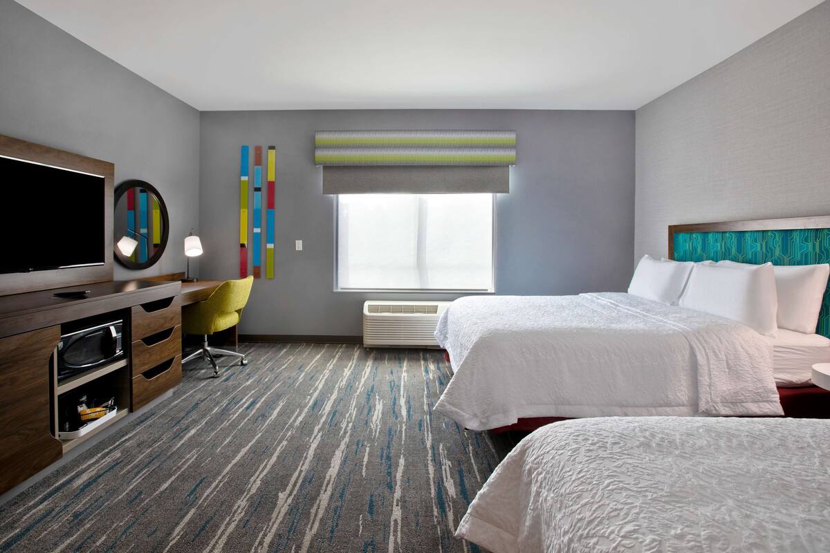 A hotel room with a large bed, a desk with a television, a chair, and a window with a view.