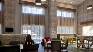 A spacious hotel lobby with a large seating area, a wooden floor, and large windows with curtains. - Hampton Inn & Suites Deptford (Woodbury)