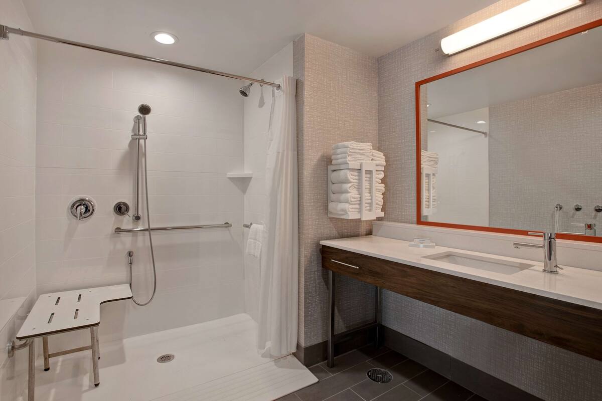 A modern bathroom with a walk-in shower, a vanity with a mirror, and a stack of towels.