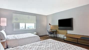 A hotel room with two beds, a desk, a chair, a TV, and a window with blinds.