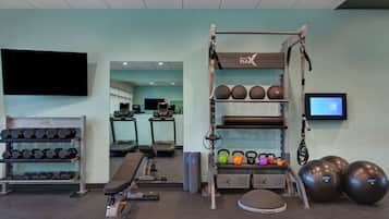 A gym with exercise equipment, treadmills, and a TV screen.