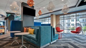 A modern lounge area with a teal sofa, small tables, hanging chairs, and a large window offering a view of buildings. - Tru By Hilton St. Petersburg Downtown Central Ave, FL (St. Petersburg)