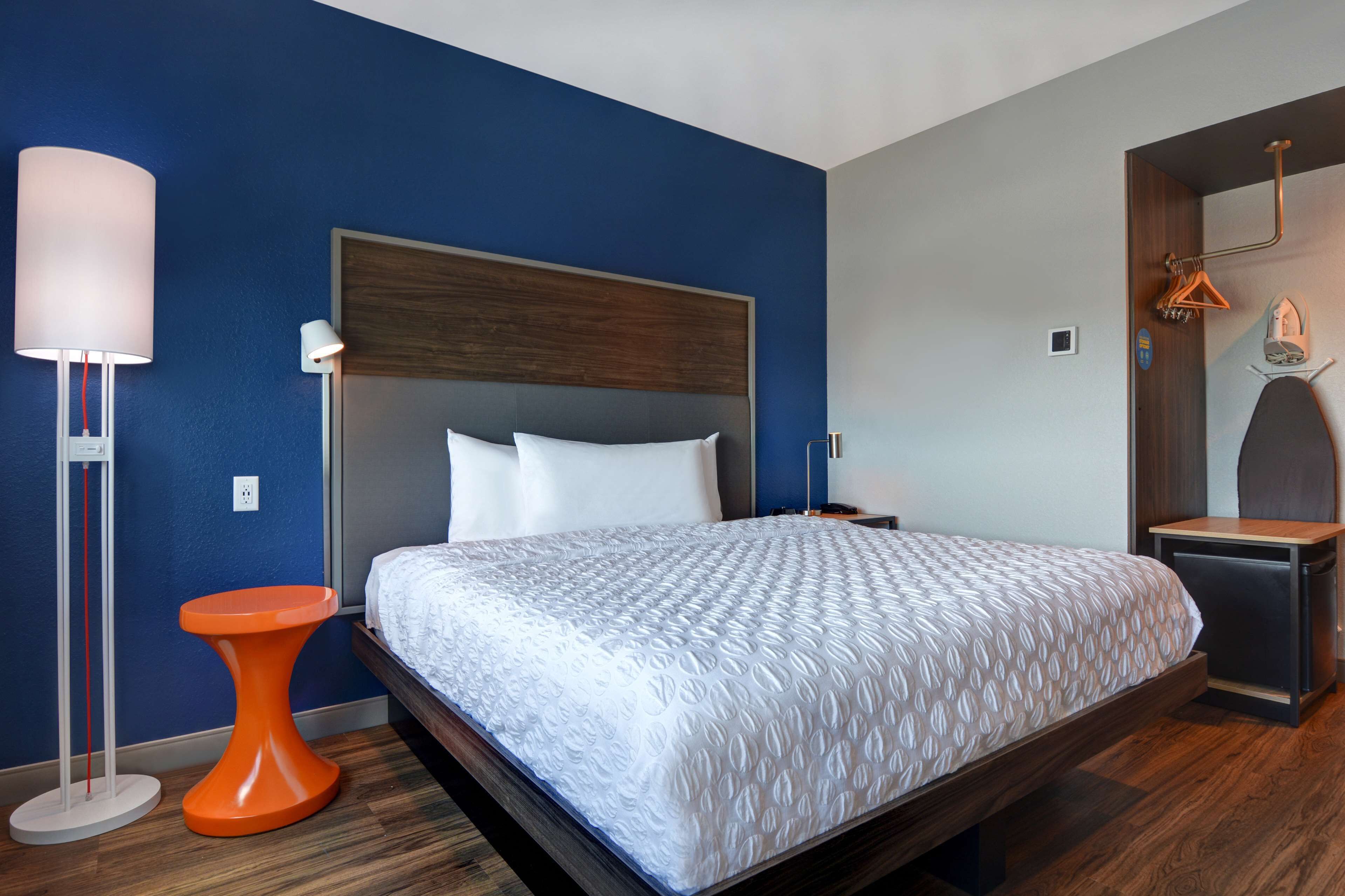 A modern hotel room with a large bed, a bedside table, a nightstand, a lamp, and a mirror.