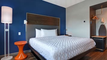 A modern hotel room with a large bed, a bedside table, a nightstand, a lamp, and a mirror.