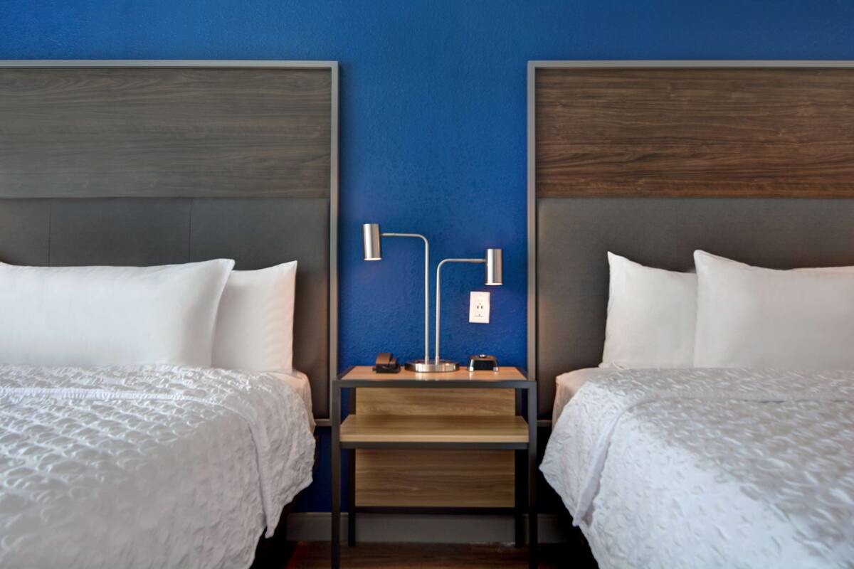 Ein Hotelzimmer mit zwei Betten, einem Nachttisch mit Lampe und einer blauen Akzentwand.