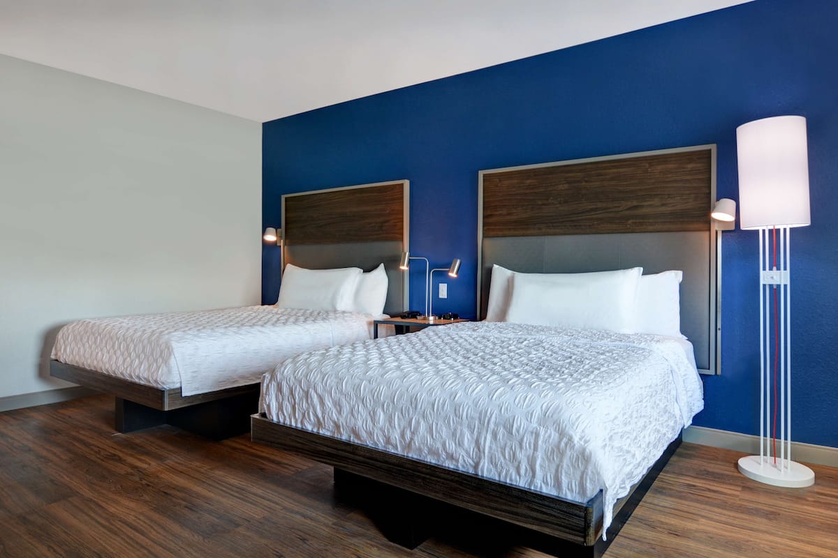 Ein Hotelzimmer mit zwei Betten, einem Nachttisch, einer Lampe und einem großen Spiegel.