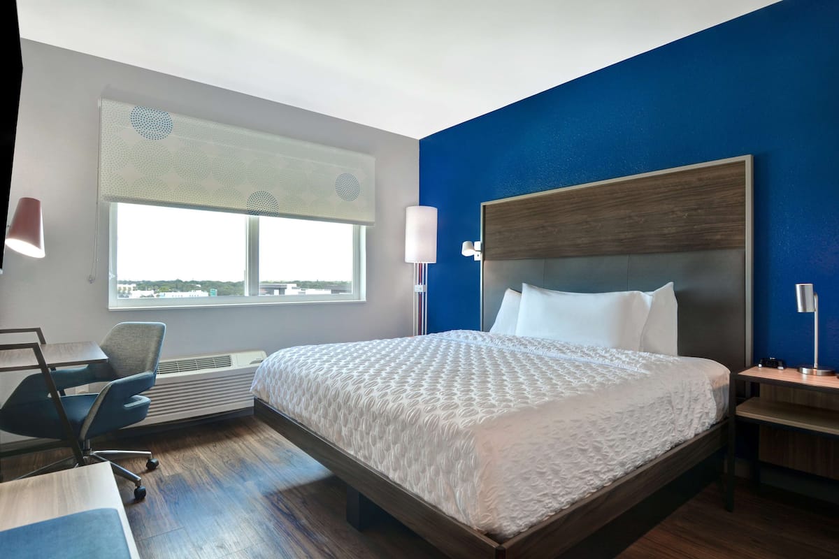 Ein Hotelzimmer mit einem großen Bett, einem Schreibtisch, einem Stuhl und einem Fenster mit Jalousien.