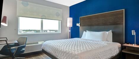 A hotel room with a large bed, a desk, a chair, and a window with blinds.