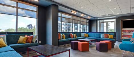 A modern lounge area with seating, tables, and large windows offering views of buildings and trees.