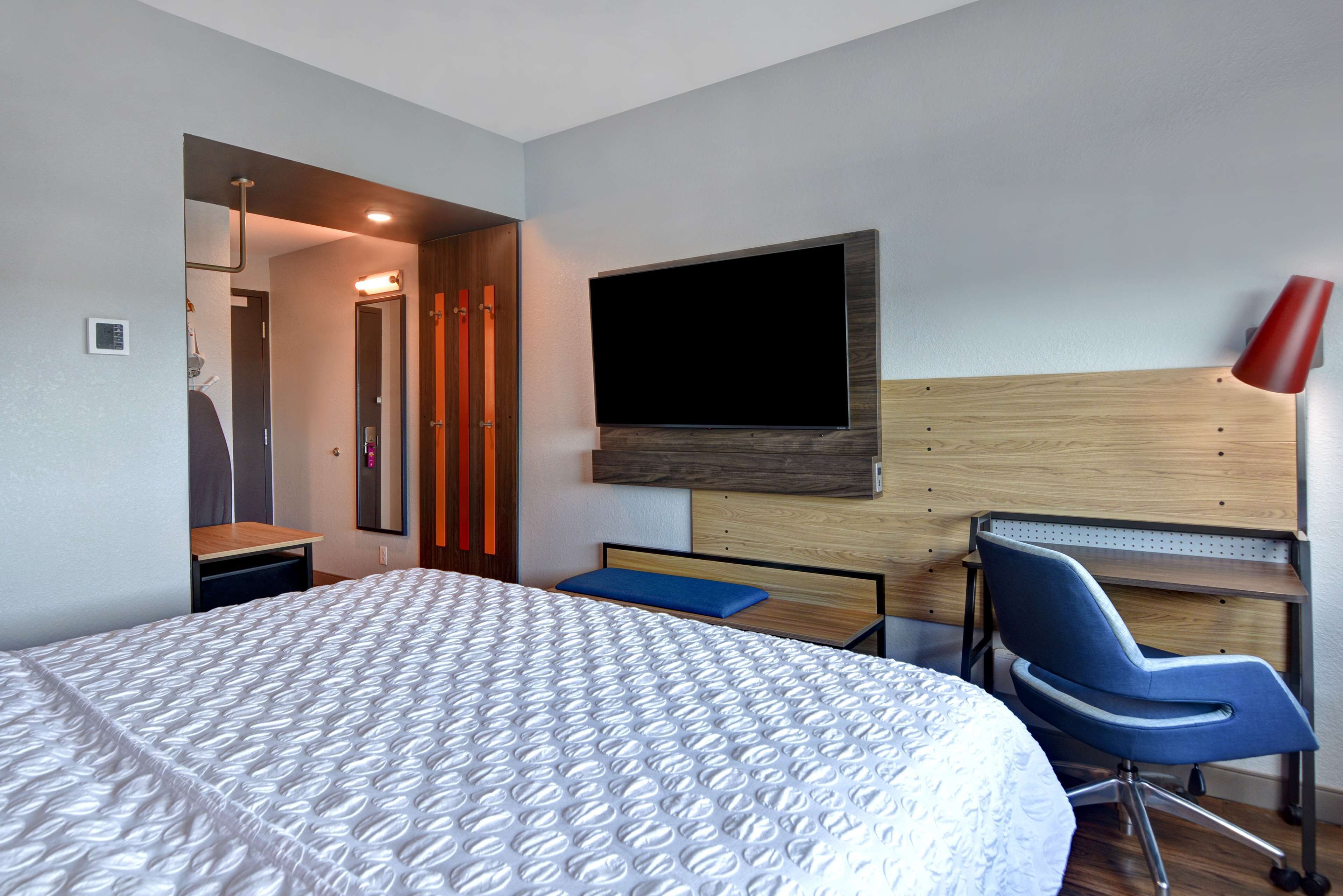 Une chambre d’hôtel moderne avec un grand lit, un bureau avec une chaise, un téléviseur fixé au mur et une lampe rouge.