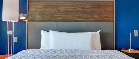 A hotel room with a large bed, a wooden headboard, and a nightstand with a lamp.
