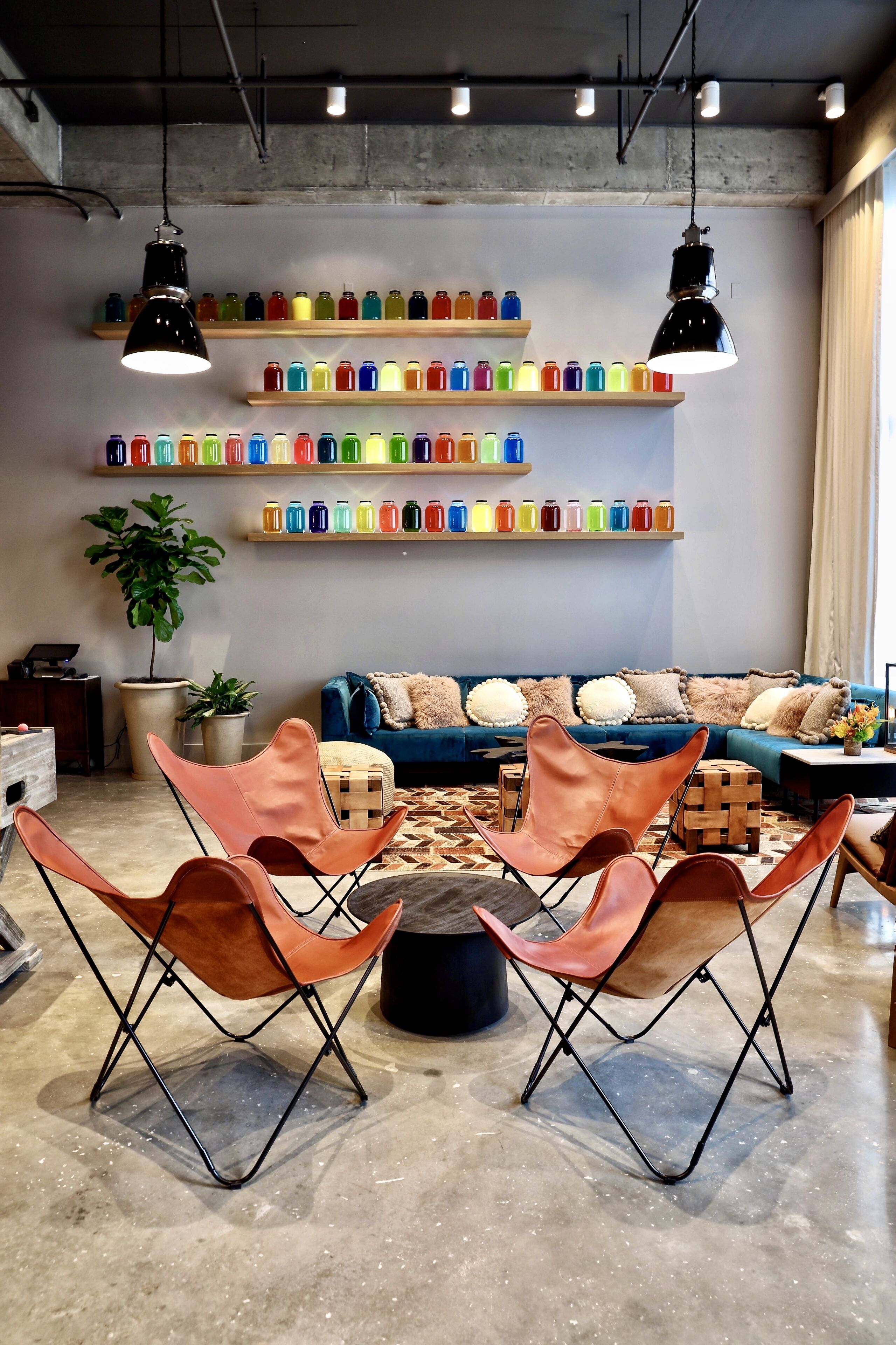 Un intérieur moderne avec un canapé, des bouteilles de boissons colorées disposées sur des étagères et des chaises originales.