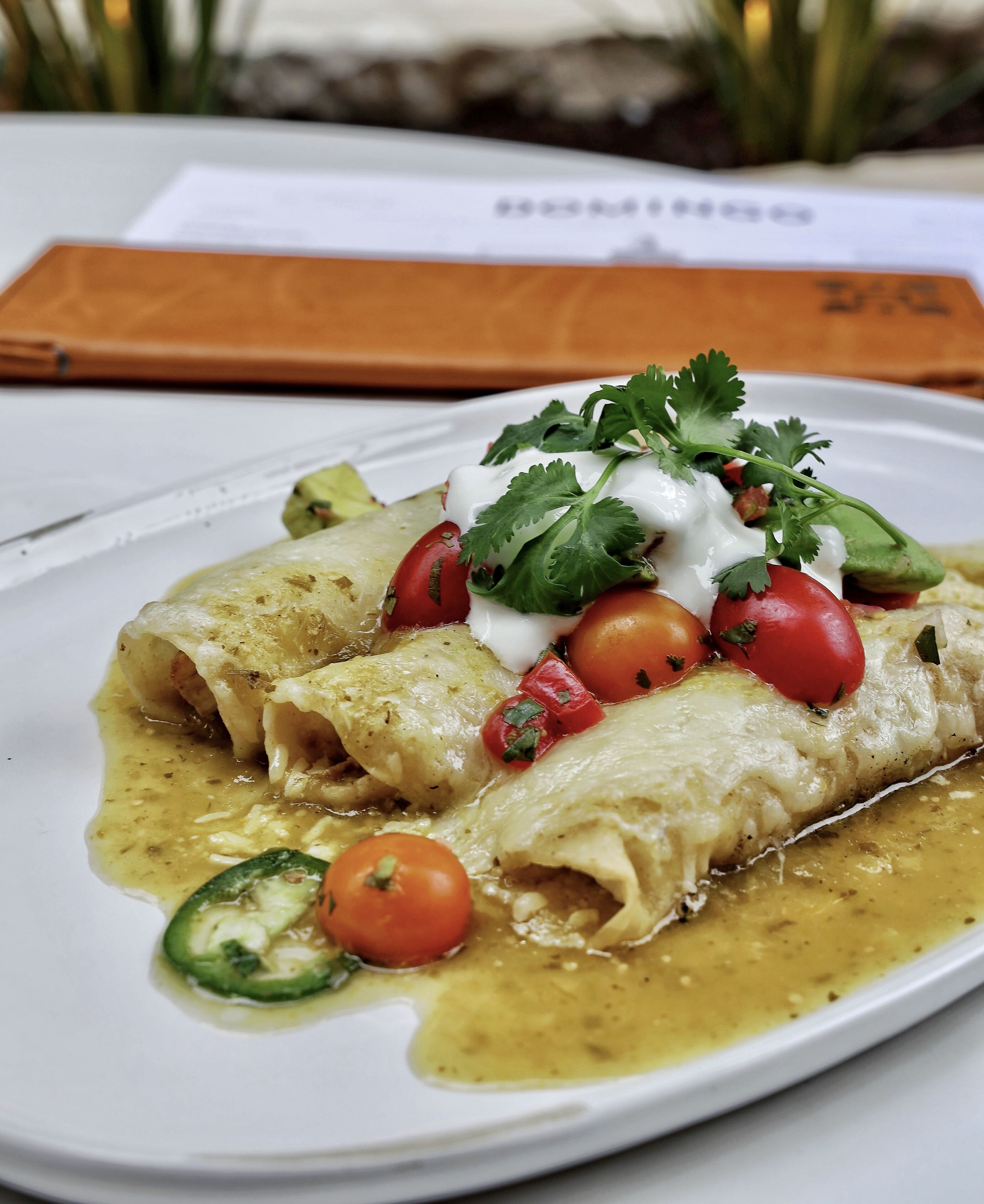 Un plato de enchiladas con crema agria, tomates y cilantro.