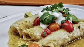 Un plato de enchiladas con crema agria, tomates y cilantro.