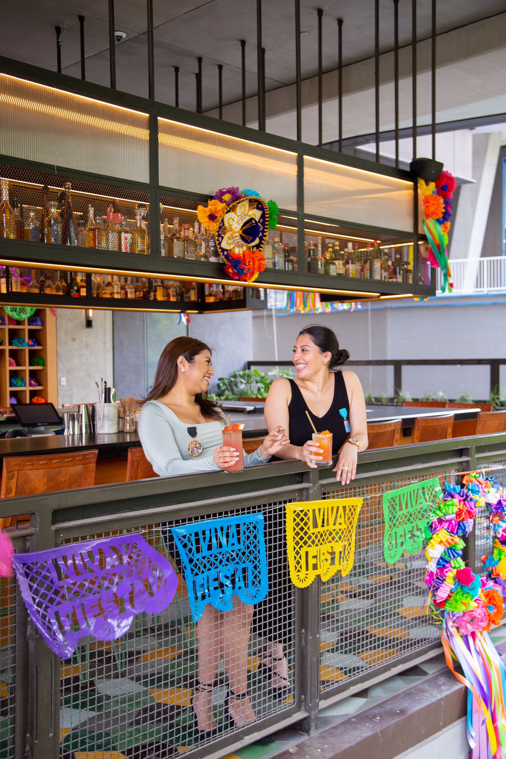 Zona de bar con un bartender y un cliente, decorada con banderines de papel de colores y un ambiente festivo.