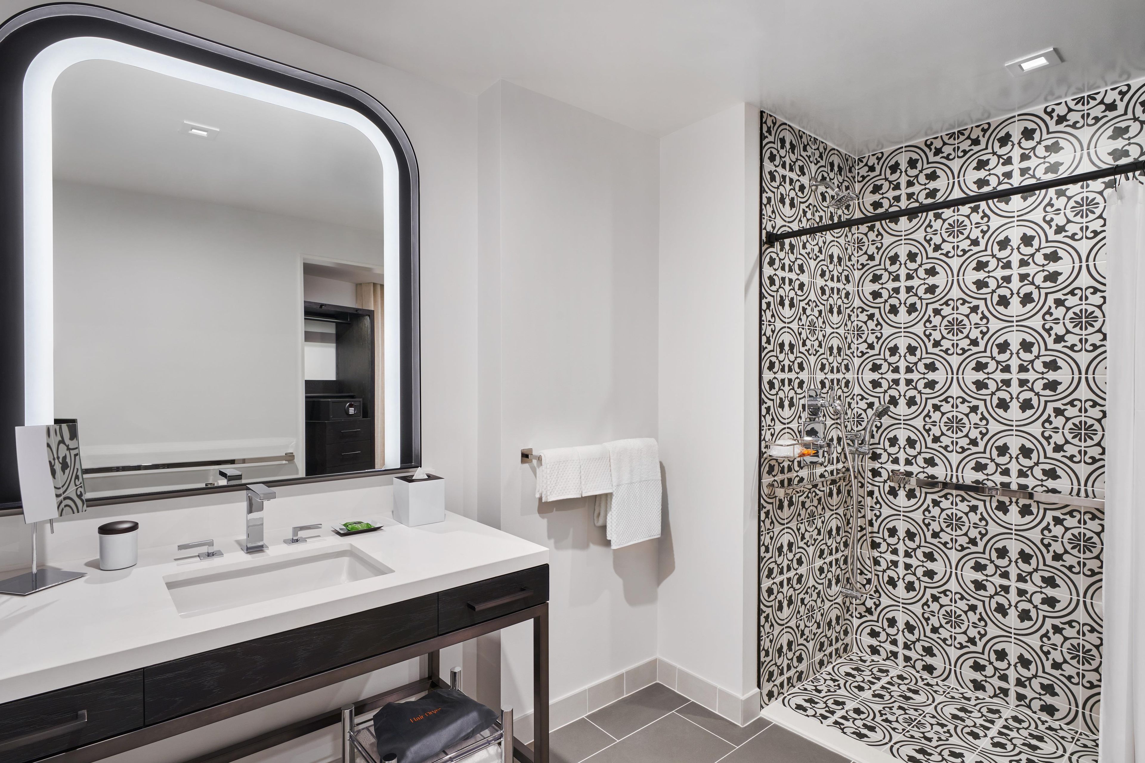 Un baño moderno con un espejo grande, un lavabo blanco y una ducha con baldosas estampadas.