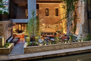 An outdoor dining area with tables and chairs, surrounded by stone walls and greenery. - Canopy San Antonio Riverwalk   (San Antonio)