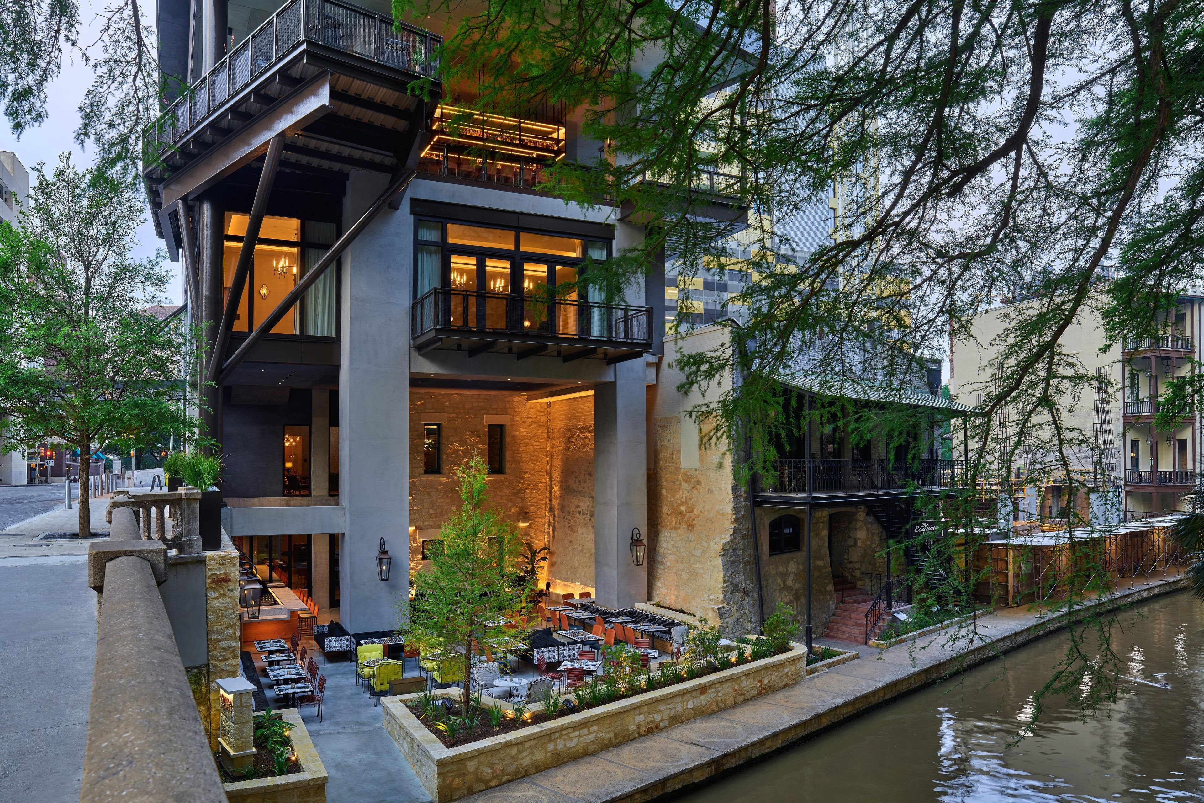 A modern building with a dining area, outdoor seating, and a water canal.