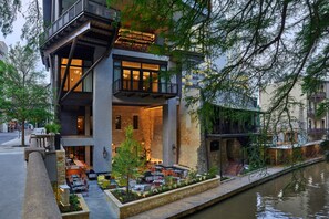 A modern building with a dining area, outdoor seating, and a water canal. - Canopy San Antonio Riverwalk   (San Antonio)
