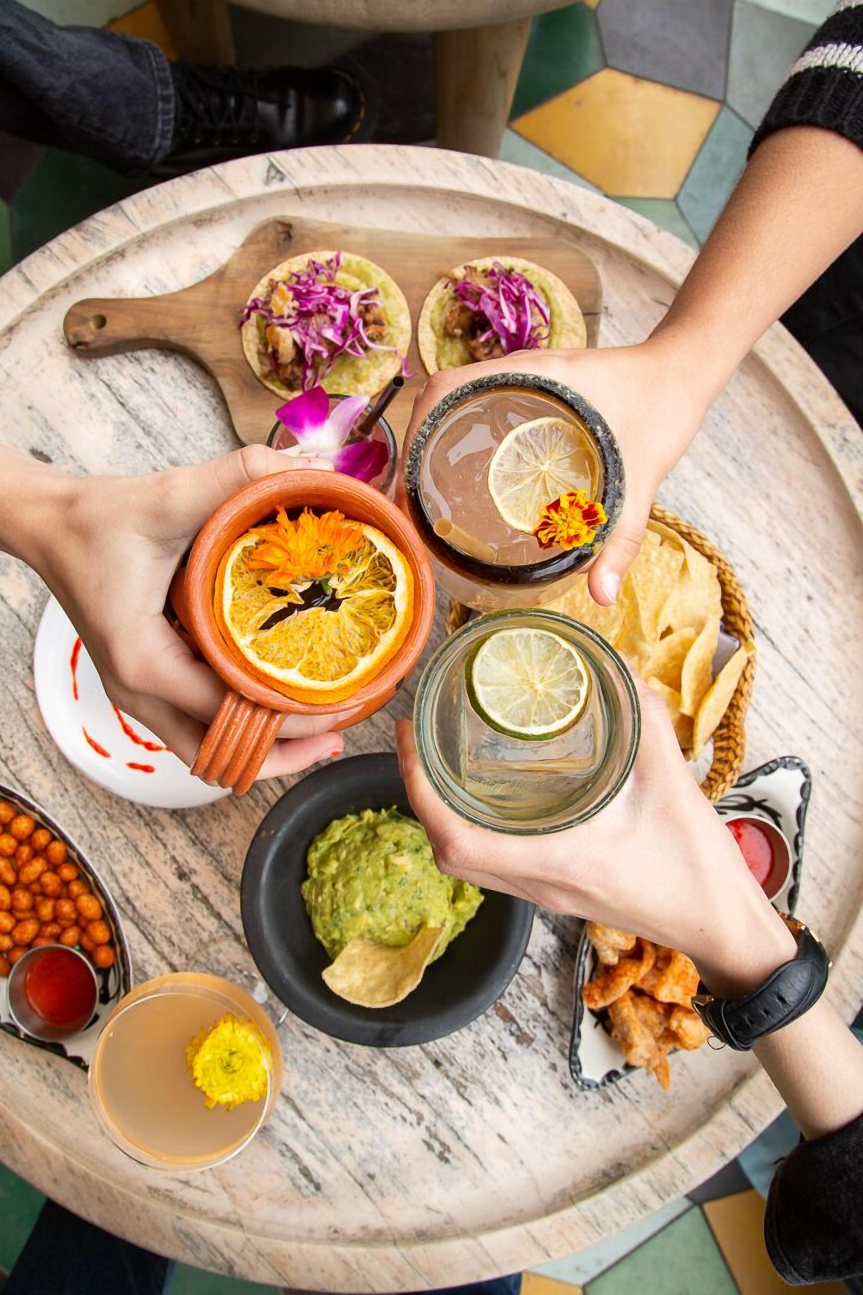 A round table with various food items and drinks, including tacos, guacamole, and a margarita.