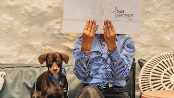 A person sitting on a couch with a dog, holding a sign that reads "San Antonio Saga."