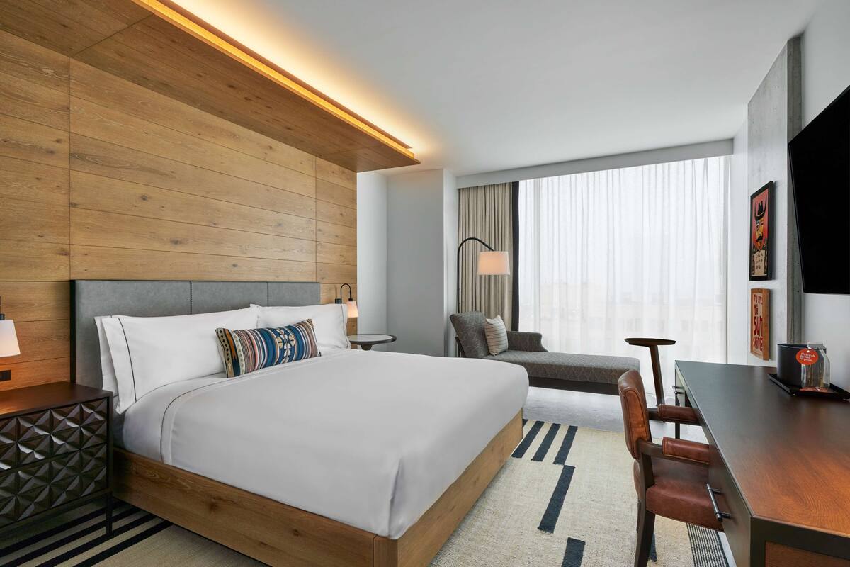 A hotel room with a large bed, a desk with a chair, a sofa, a lamp, and a TV.