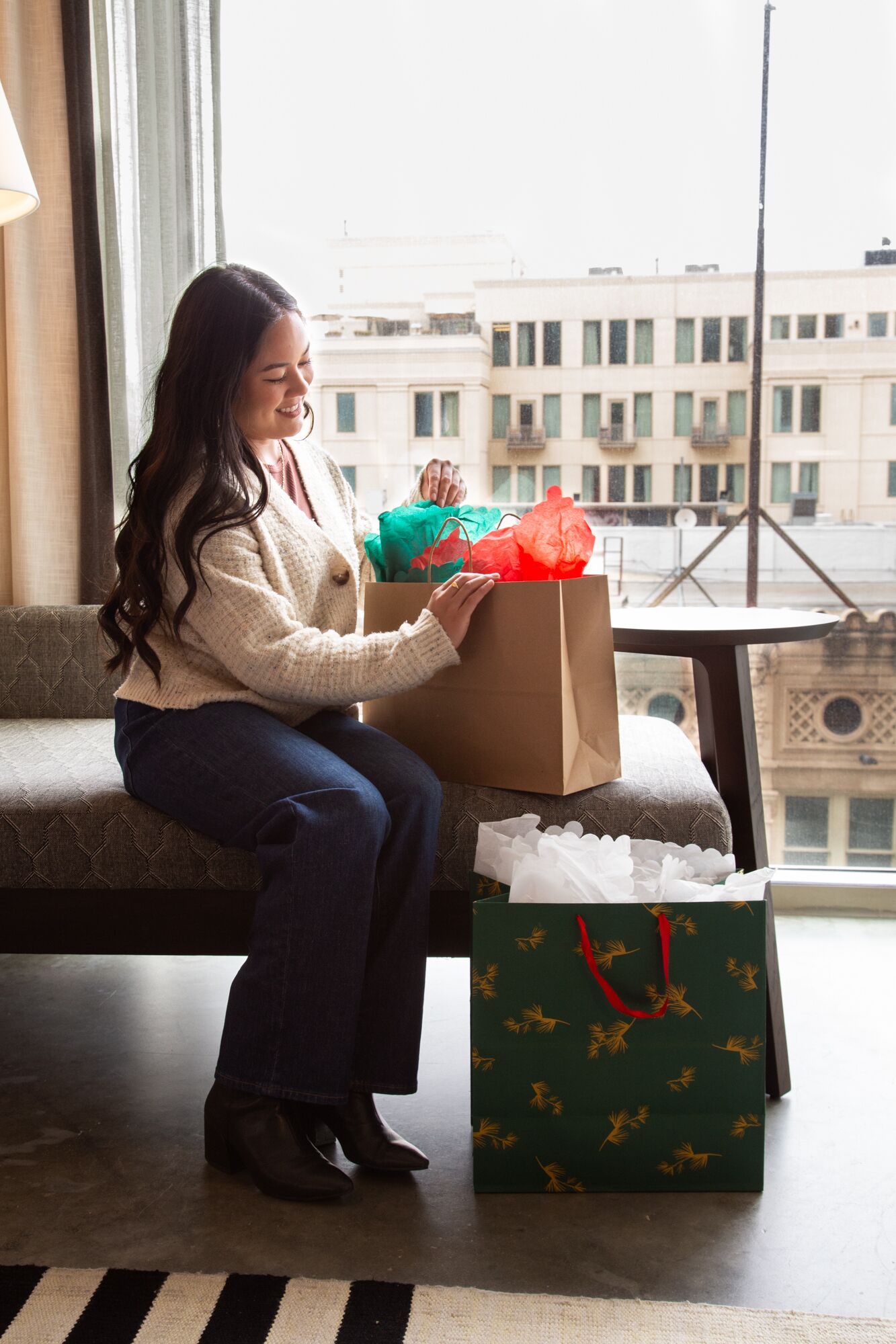 A person sitting on a sofa with a large gift box and a green shopping bag with a red handle.
