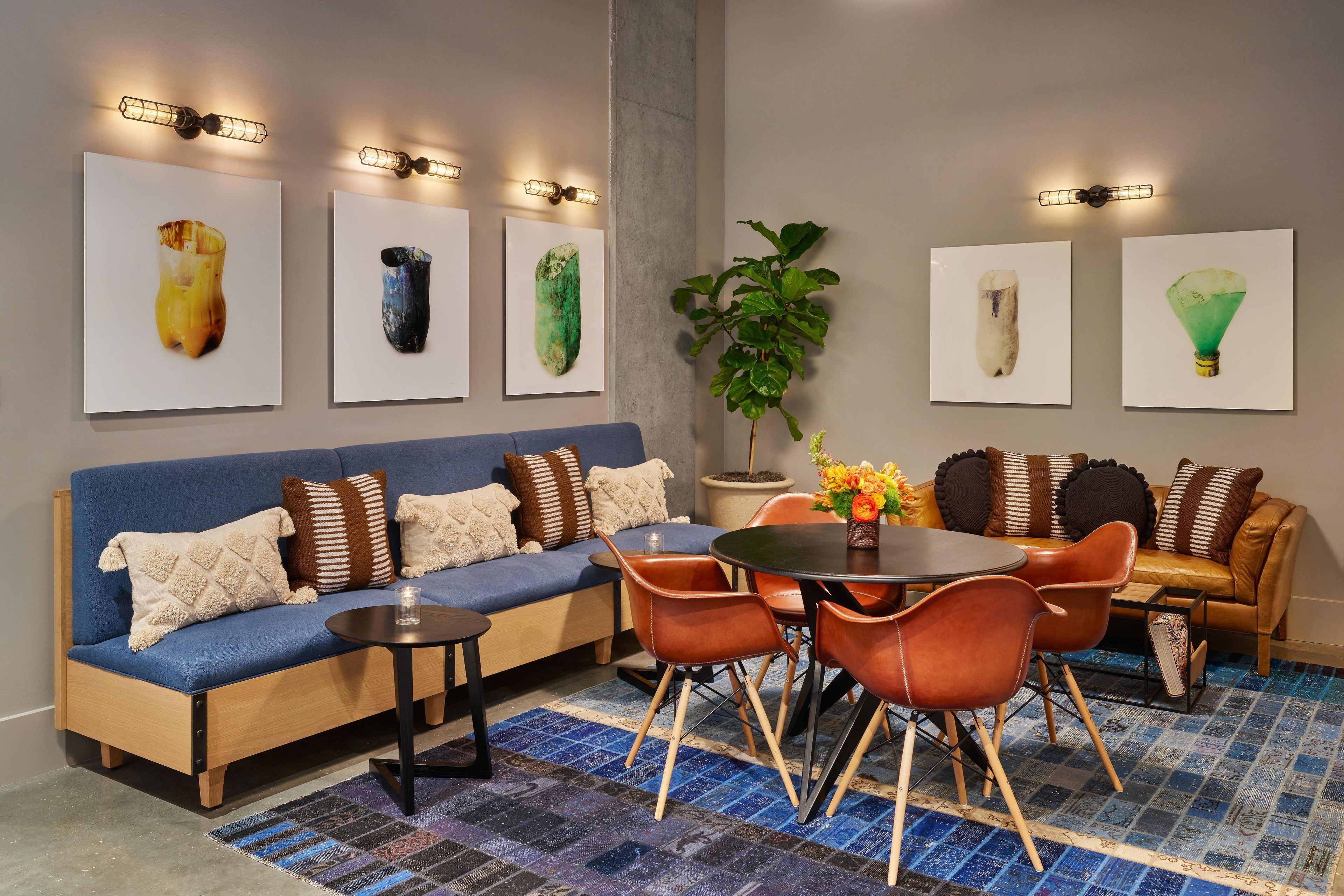 Un salon moderne avec un canapé bleu, une table ronde et des chaises orange. Quatre œuvres d’art encadrées ornent le mur.