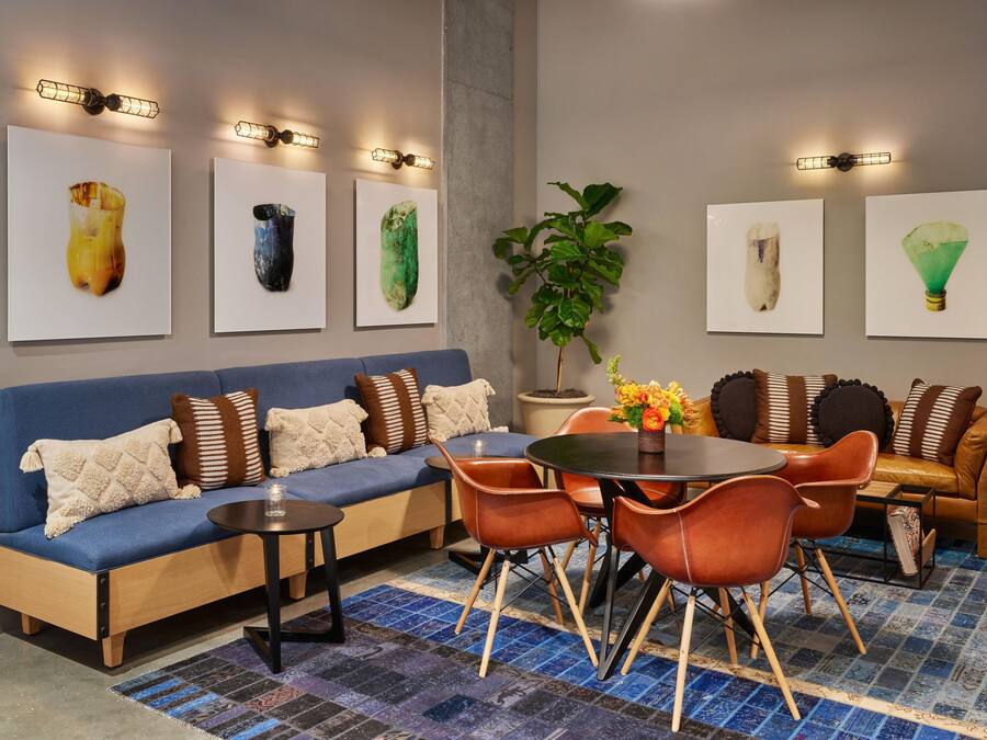 Un salon moderne avec un canapé bleu, une table ronde et des chaises orange. Quatre œuvres d’art encadrées ornent le mur.