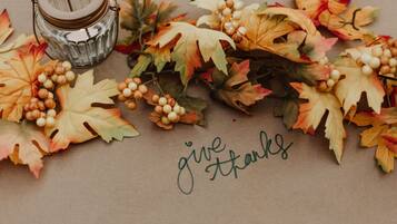 A decorative arrangement with autumn leaves and a candle, and the phrase "give thanks" written on a brown background.