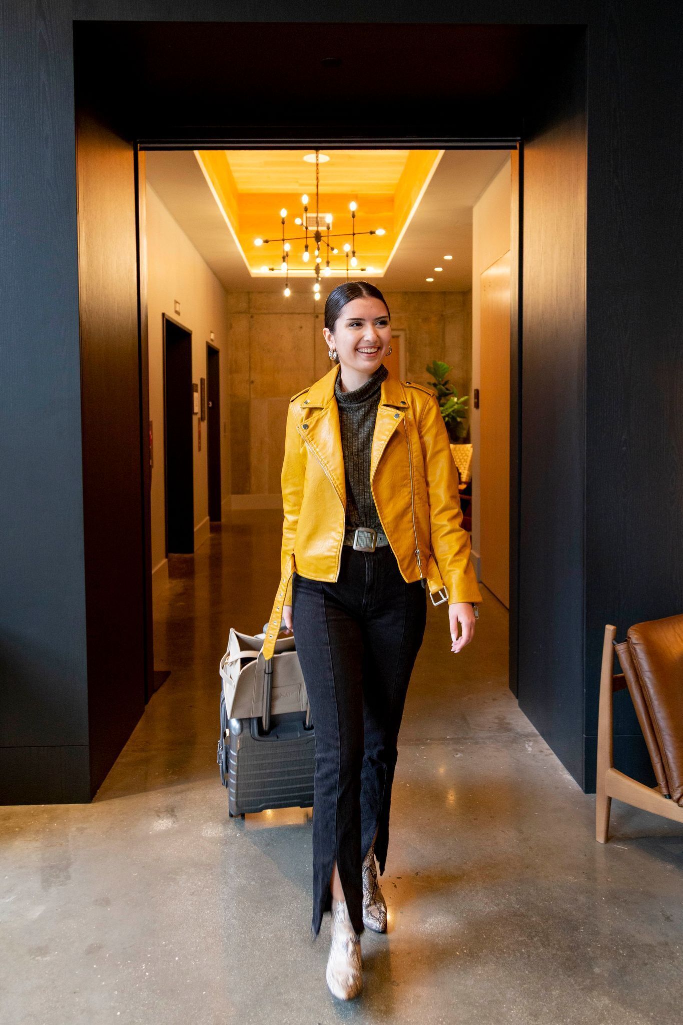 A modern hotel corridor with a wooden floor, a black wall, and a ceiling with a light fixture.