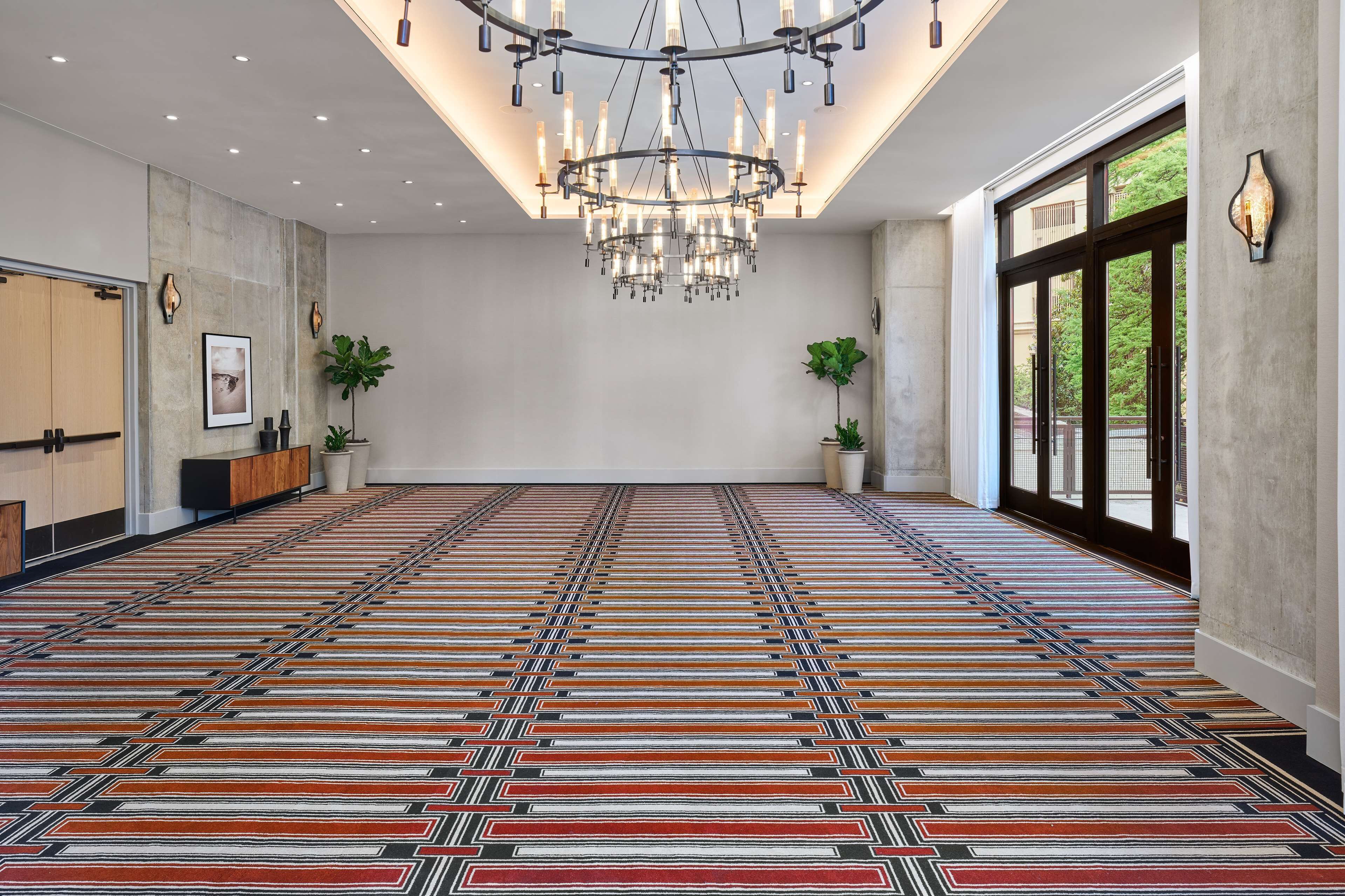 Una habitación amplia con alfombra estampada, un gran candelabro y plantas en macetas.
