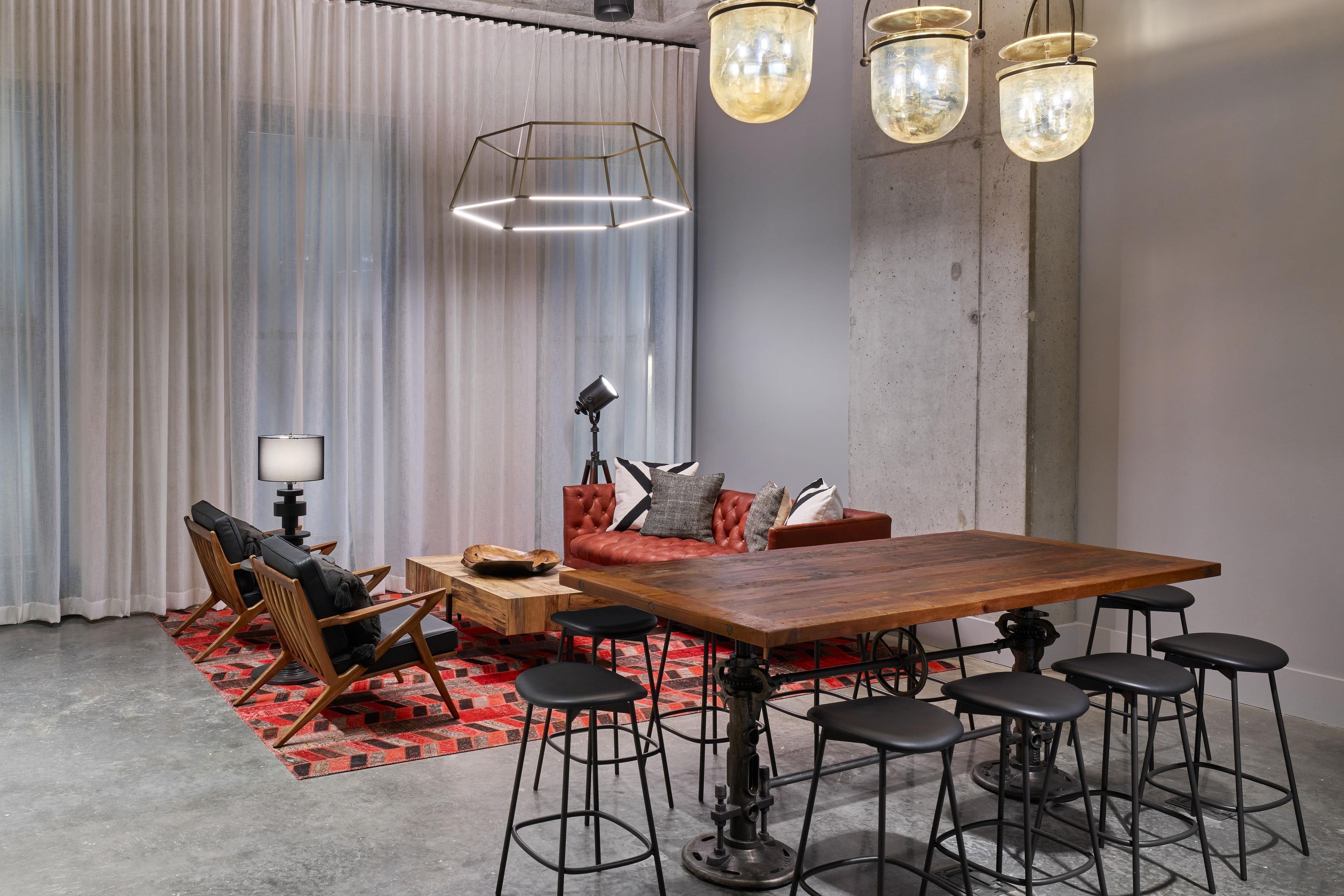A modern dining area with a wooden table, black bar stools, and a red sofa with patterned cushions.
