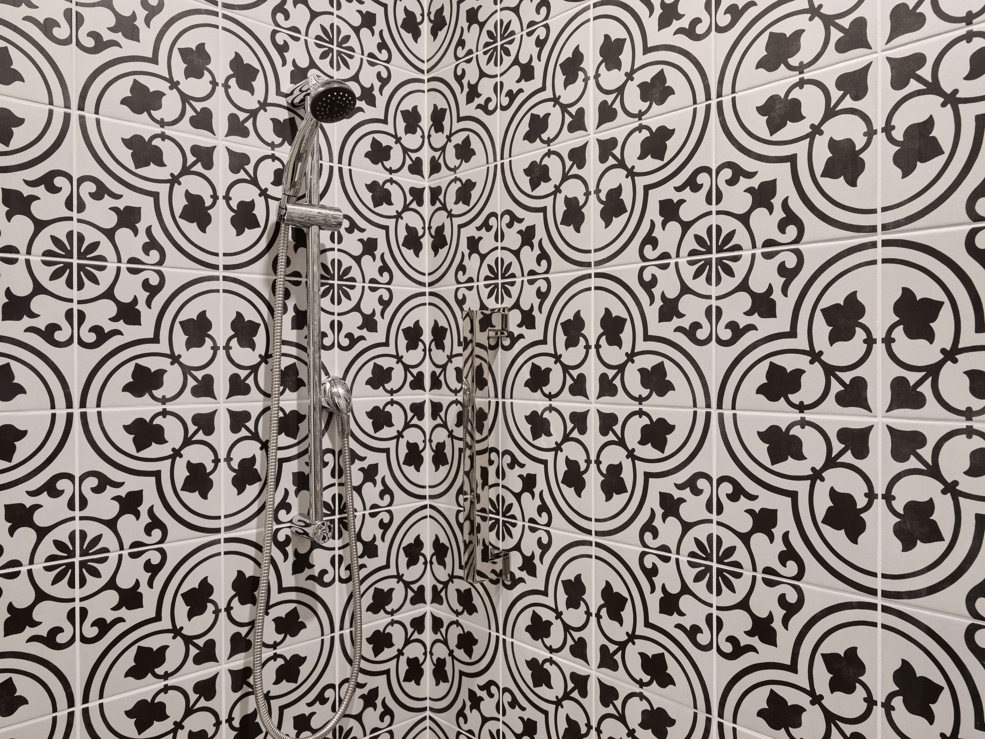 Une salle de bain avec des carreaux aux motifs noir et blanc et une douche équipée d’un pommeau de douche à main.