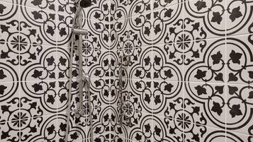 Une salle de bain avec des carreaux aux motifs noir et blanc et une douche équipée d’un pommeau de douche à main.