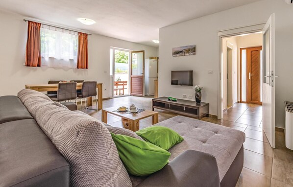 A modern living room with a sofa, coffee table, and TV. There is a dining area with chairs and a table, and a kitchen area with a fridge and oven. - Beautiful home in Pazin (Pazin)