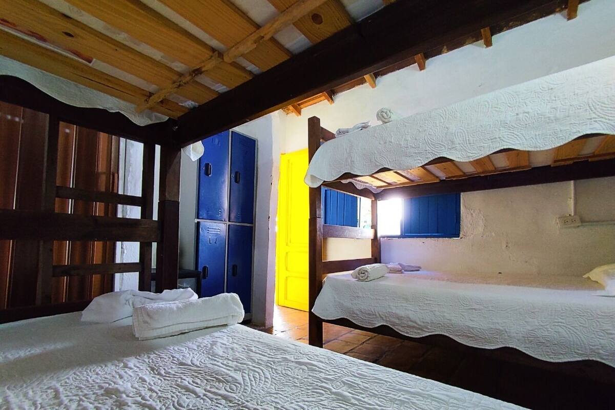 Une chambre avec deux lits, des poutres en bois, une porte bleue et un mur jaune.
