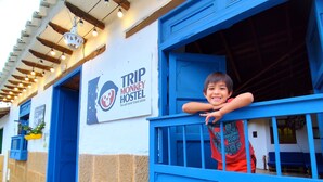 Een hostel met een bord waarop staat 'TRIP MONKEY HOSTEL' en een kind dat uit een raam kijkt.