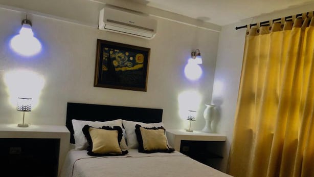 A bedroom with a bed, two bedside tables, a nightstand, an air conditioner, a painting, and a curtain. - Casa Don Arturo (Santa Marta)