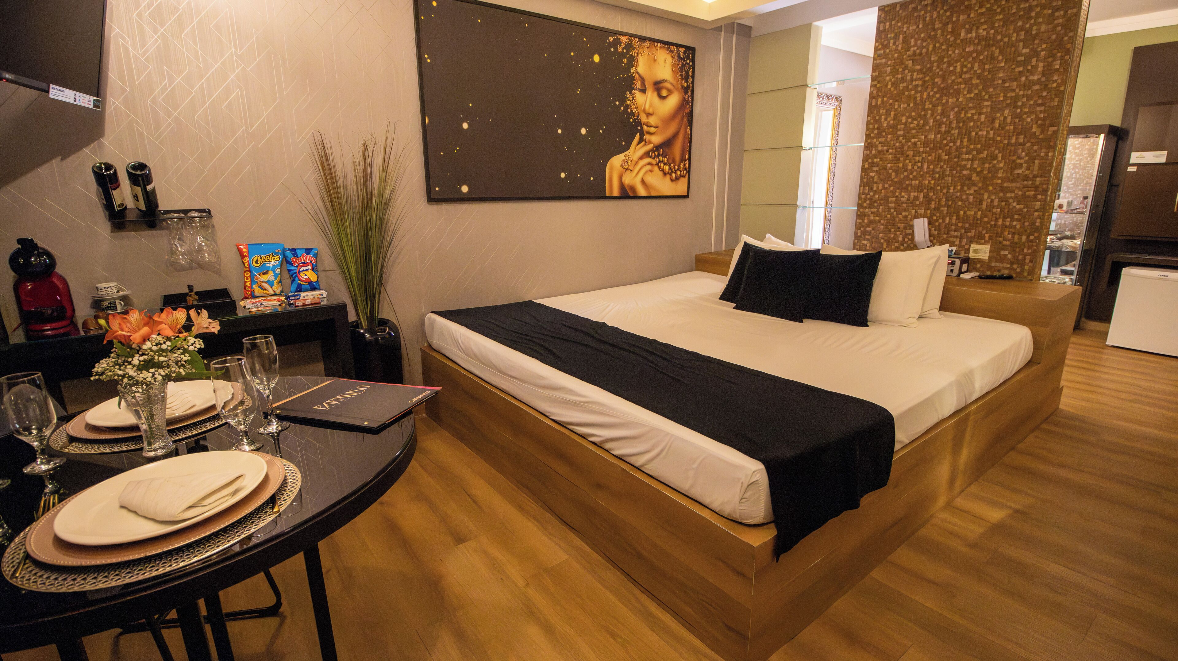Ein Hotelzimmer mit Bett, einem Esstisch mit Blumenvase und einem Bild an der Wand.