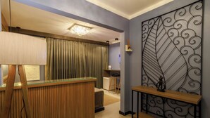 A hotel reception area with a wooden reception desk, a chandelier, a decorative metal partition, and a small statue on a console table.