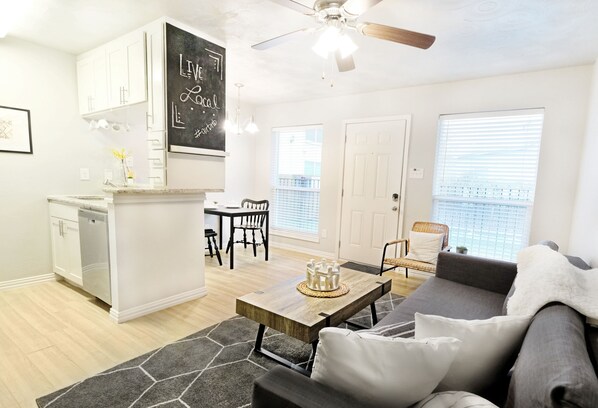A modern living room with a gray sofa, a wooden coffee table, and a dining area with a white table and chairs.