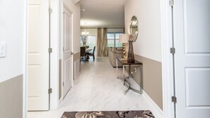 A hallway with a dining area in the background, a lamp, and a mirror on the wall.